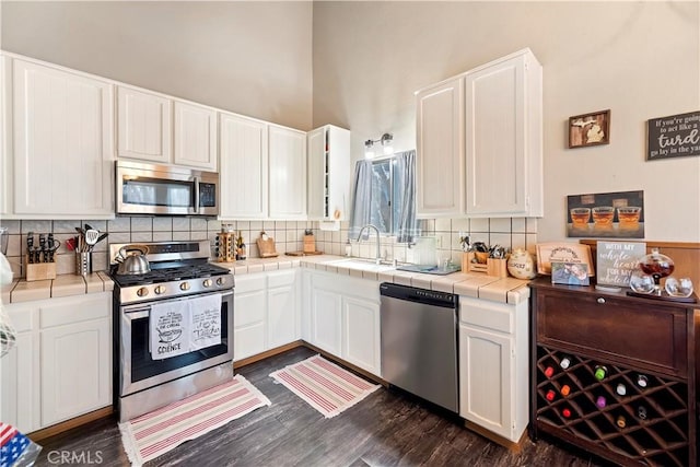 kitchen with white cabinetry, tasteful backsplash, tile counters, stainless steel appliances, and dark wood-style floors