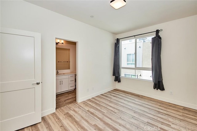unfurnished bedroom featuring baseboards, ensuite bathroom, light wood-style flooring, and a sink