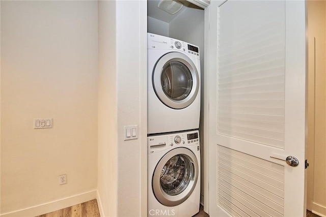 clothes washing area featuring stacked washer and dryer, wood finished floors, laundry area, and baseboards