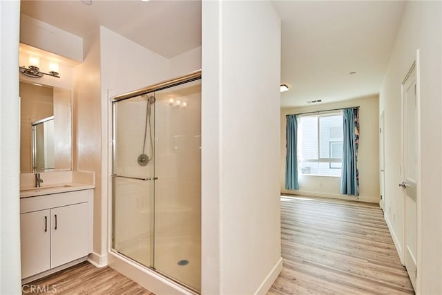 bathroom with baseboards, wood finished floors, a shower stall, and vanity