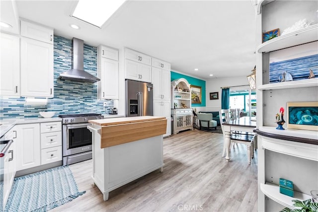 kitchen featuring wall chimney range hood, white cabinetry, and stainless steel appliances