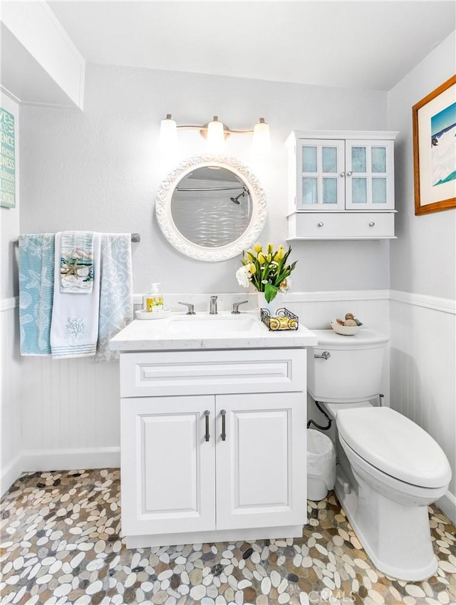 bathroom featuring vanity, toilet, and a wainscoted wall