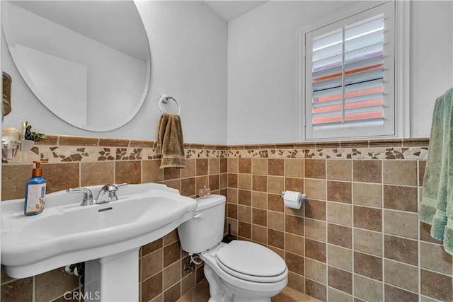 half bath with toilet, tile walls, a sink, and wainscoting