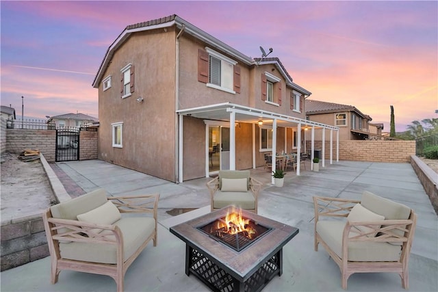 rear view of property featuring fence, an outdoor living space with a fire pit, a gate, a patio area, and stucco siding