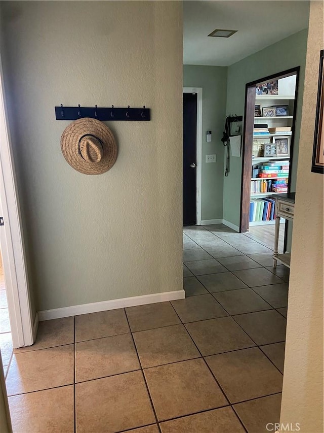 corridor featuring baseboards, tile patterned flooring, and a textured wall