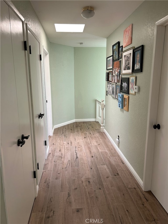 hallway featuring a textured wall, wood finished floors, and baseboards