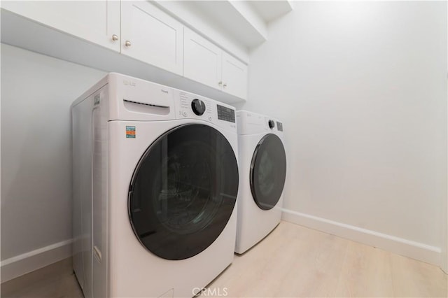 laundry area with light wood-style floors, baseboards, cabinet space, and washer and dryer