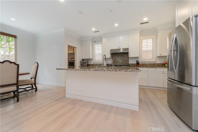 kitchen with freestanding refrigerator, white cabinetry, light wood-type flooring, under cabinet range hood, and visible vents