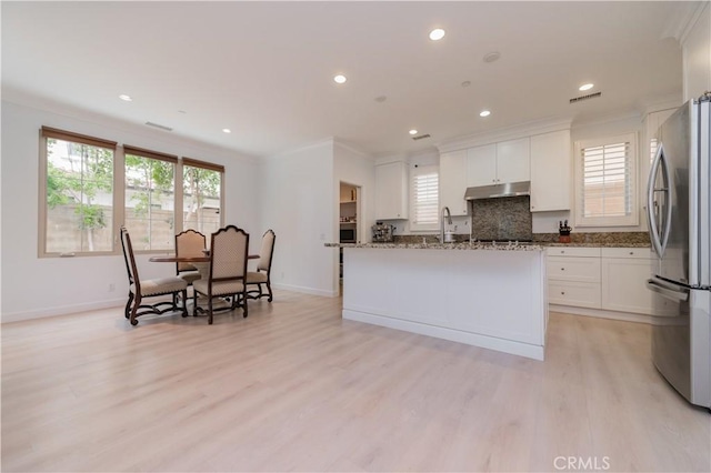 kitchen featuring baseboards, freestanding refrigerator, under cabinet range hood, and a wealth of natural light