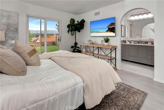 bedroom with visible vents, light wood-style floors, ensuite bathroom, access to outside, and a sink
