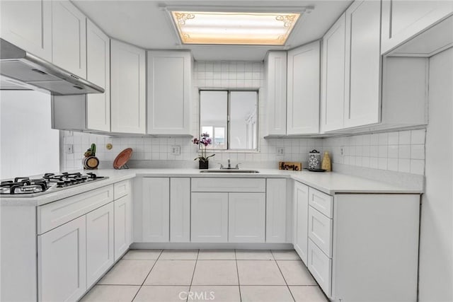 kitchen with white cabinets, a sink, light countertops, stainless steel gas stovetop, and under cabinet range hood