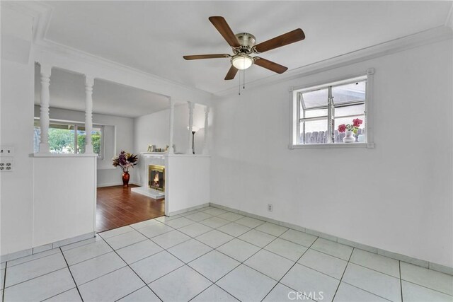 unfurnished room with ceiling fan, crown molding, light tile patterned floors, baseboards, and a glass covered fireplace