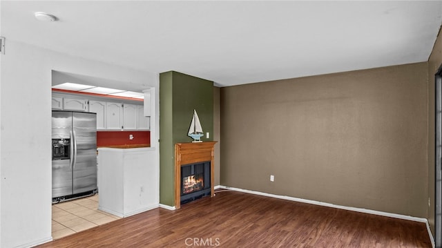 unfurnished living room featuring baseboards, a glass covered fireplace, and light wood-type flooring