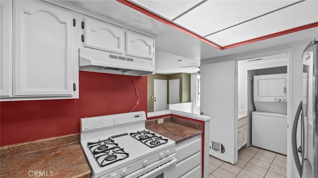 kitchen with stacked washer and clothes dryer, light tile patterned flooring, gas range gas stove, under cabinet range hood, and white cabinets