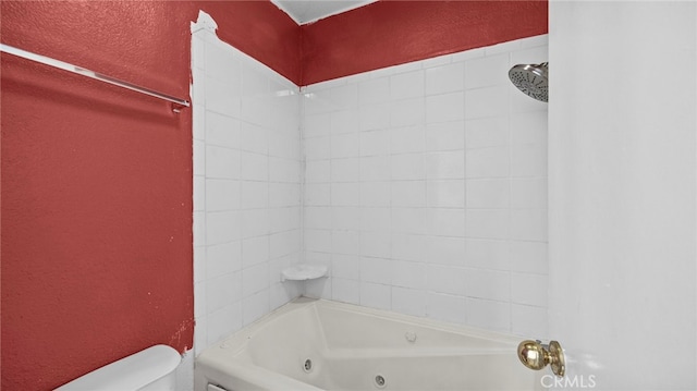 bathroom featuring a textured wall, a combined bath / shower with jetted tub, and toilet