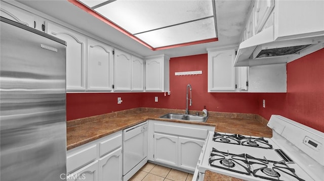 kitchen with dark countertops, a sink, white cabinets, under cabinet range hood, and white appliances
