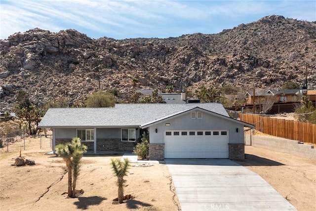 ranch-style house with fence, driveway, stone siding, a mountain view, and an attached garage