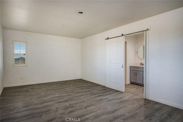 unfurnished bedroom with wood finished floors, ensuite bathroom, and baseboards