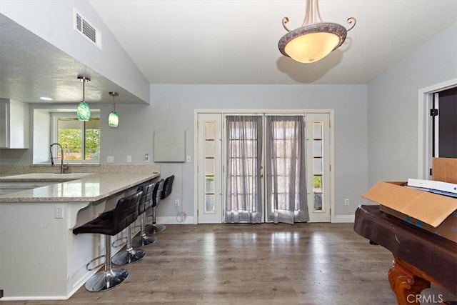 kitchen featuring visible vents, light stone counters, wood finished floors, and baseboards