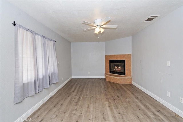 unfurnished living room with wood finished floors, a tile fireplace, baseboards, visible vents, and a ceiling fan