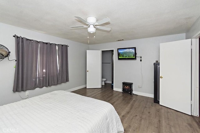 bedroom featuring a wood stove, visible vents, wood finished floors, and baseboards