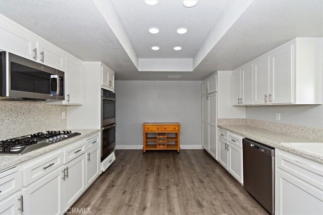 kitchen featuring white cabinets, appliances with stainless steel finishes, a tray ceiling, baseboards, and wood finished floors