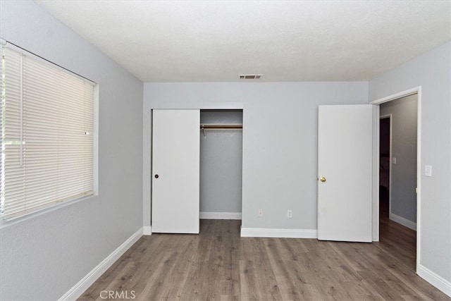 unfurnished bedroom with baseboards, visible vents, wood finished floors, and a closet