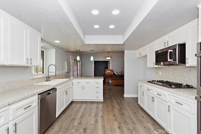 kitchen with white cabinetry, a sink, light wood-style floors, stainless steel appliances, and a peninsula