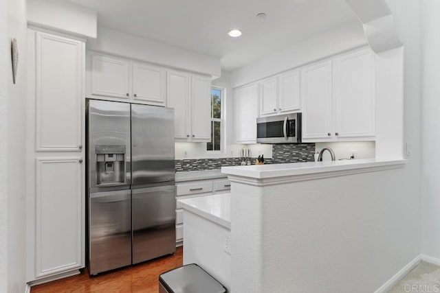 kitchen with tasteful backsplash, white cabinets, stainless steel appliances, light countertops, and recessed lighting