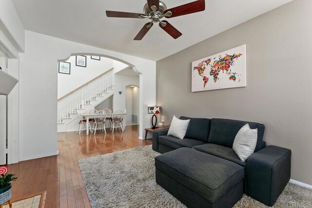 living area featuring arched walkways, ceiling fan, wood-type flooring, baseboards, and stairway