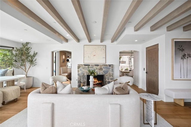 living room with beamed ceiling, baseboards, arched walkways, light wood finished floors, and a stone fireplace