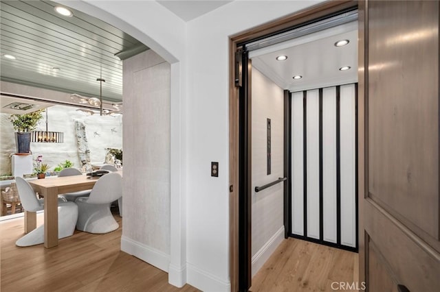 hallway with elevator, baseboards, light wood-style flooring, and arched walkways
