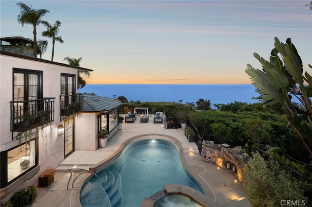 pool at dusk featuring a pool with connected hot tub, a water view, and a patio area