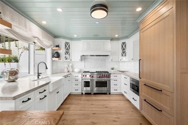 kitchen featuring open shelves, custom range hood, appliances with stainless steel finishes, light wood finished floors, and a sink
