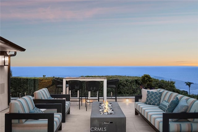 balcony at dusk featuring a patio, a water view, and an outdoor living space with a fire pit
