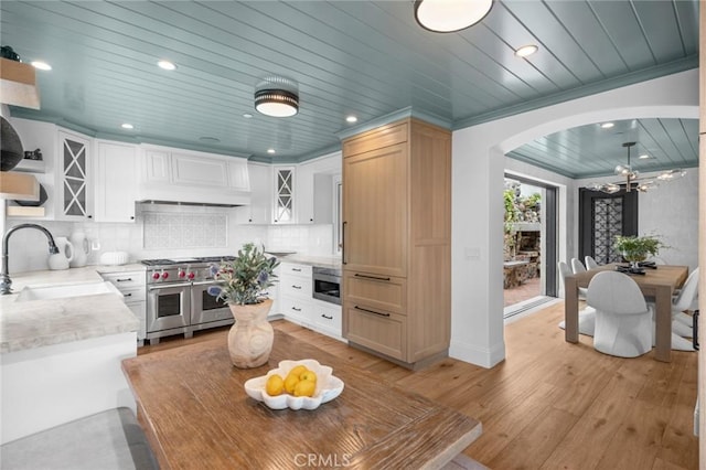 kitchen with a sink, wooden ceiling, range with two ovens, light wood-style flooring, and arched walkways