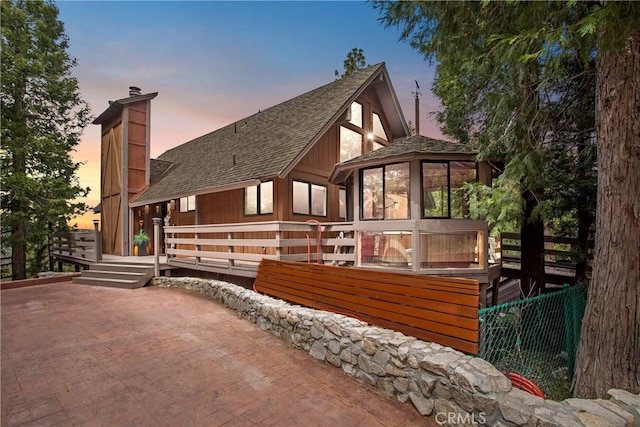 825 Grass Valley Rd, Lake Arrowhead, CA 92352 - property exterior at dusk with a patio, a deck, a chimney, a shingled roof, and a sunroom