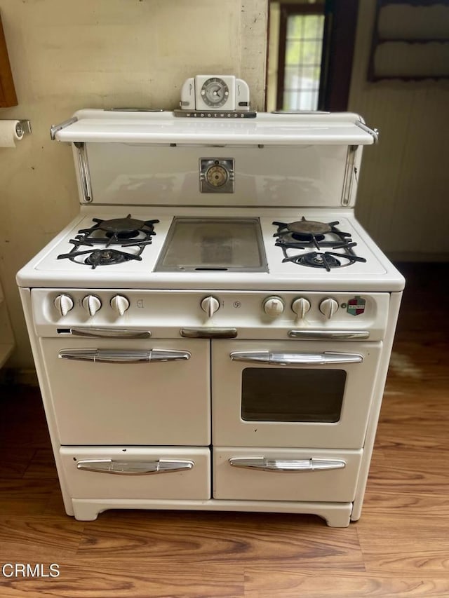 interior details featuring double oven range, wood finished floors, and white cabinets