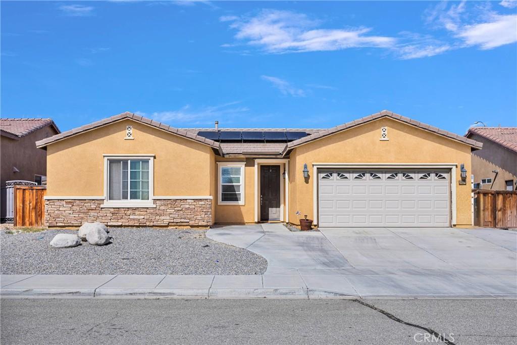 ranch-style house featuring concrete driveway, stone siding, solar panels, stucco siding, and a garage