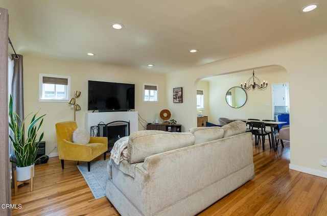 living area with light wood finished floors, recessed lighting, a chandelier, a fireplace, and arched walkways