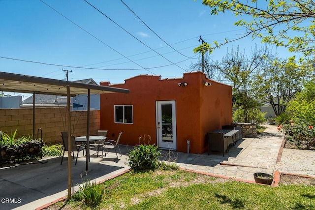rear view of house with a patio, stucco siding, and fence
