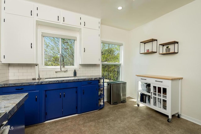 kitchen with blue cabinets, decorative backsplash, white cabinets, a sink, and baseboards