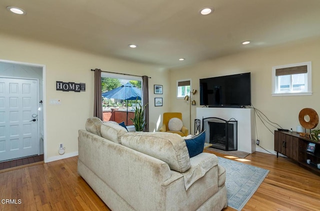 living room featuring wood finished floors, a fireplace with raised hearth, and recessed lighting