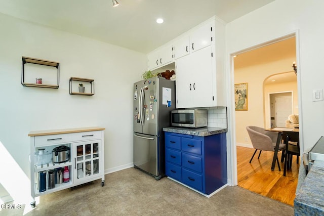 kitchen with white cabinets, appliances with stainless steel finishes, blue cabinets, baseboards, and arched walkways