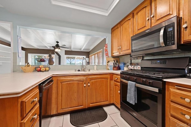 kitchen with brown cabinets, a sink, tasteful backsplash, light countertops, and appliances with stainless steel finishes