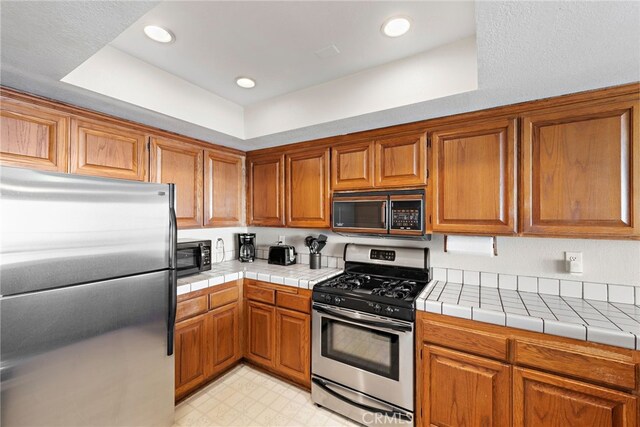 411 Avenida Granada Unit 4F, San Clemente, CA 92672 - kitchen with stainless steel appliances, brown cabinets, light floors, tile counters, and recessed lighting