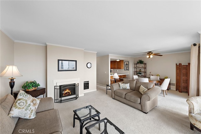 living room with ornamental molding, a warm lit fireplace, ceiling fan, and light colored carpet