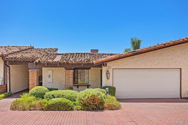 view of front of property featuring a garage, a tiled roof, stucco siding, and decorative driveway