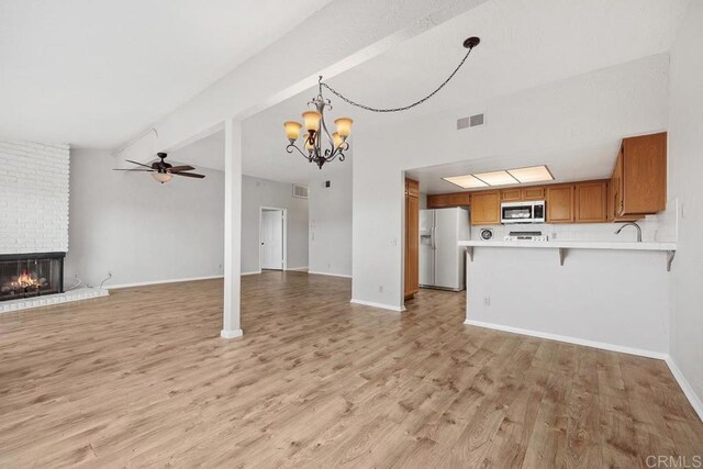 unfurnished living room featuring visible vents, a brick fireplace, baseboards, ceiling fan with notable chandelier, and light wood-style floors