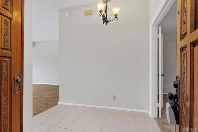 interior space featuring baseboards, a textured wall, light tile patterned floors, and a notable chandelier
